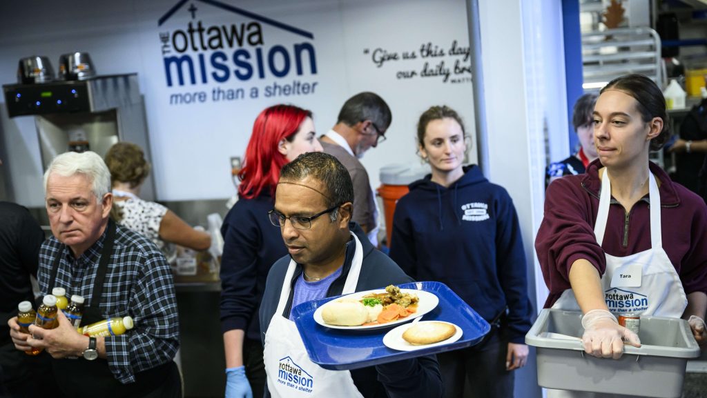 Volunteers distribute Thanksgiving meals to clients seated in the dining hall at the Ottawa Mission in Ottawa