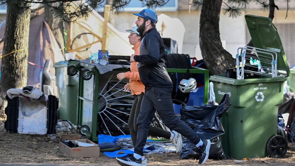 People jog by a homeless encampment.